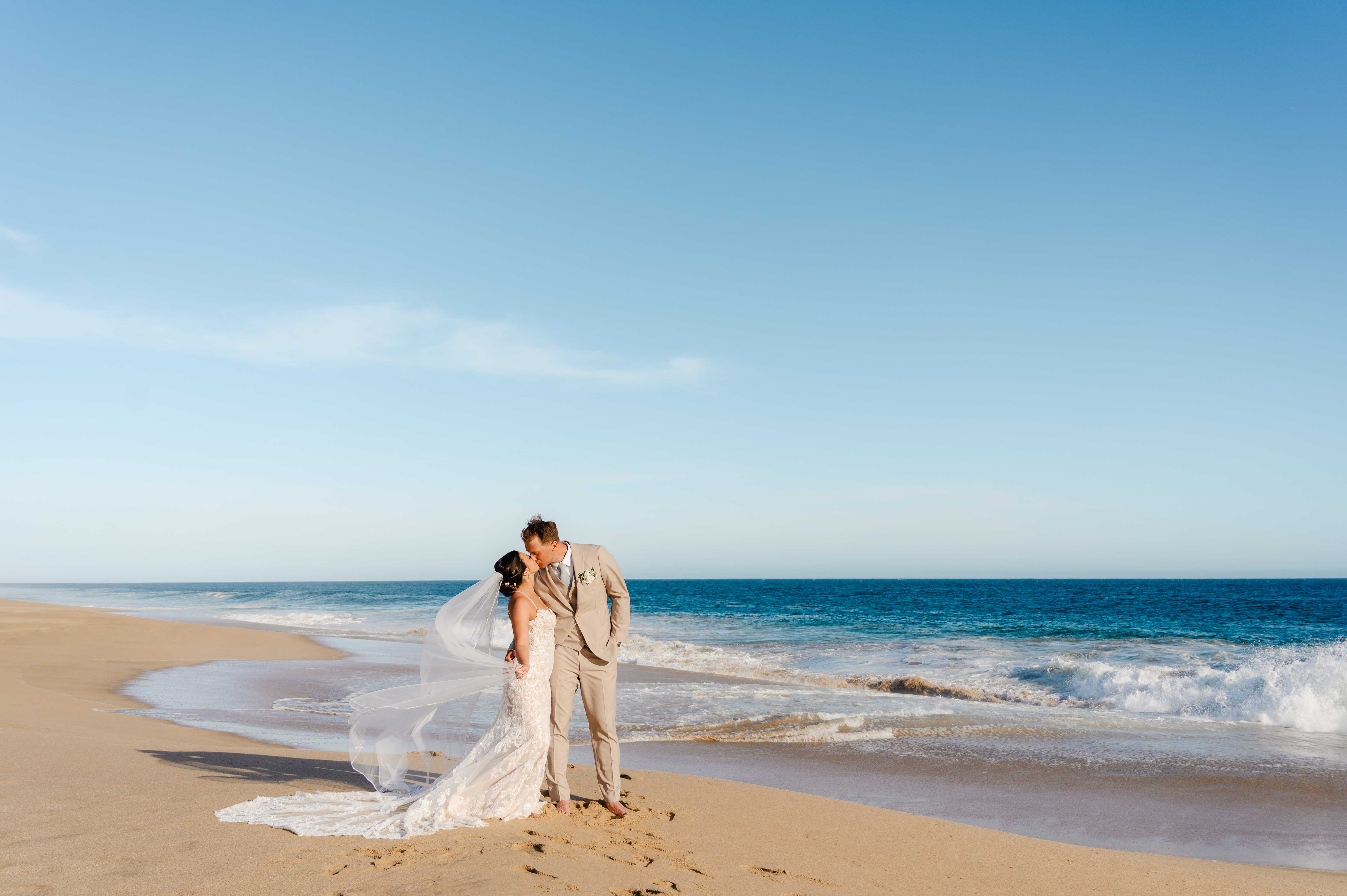 Romantic beach wedding couple with flowing veil on pristine sand