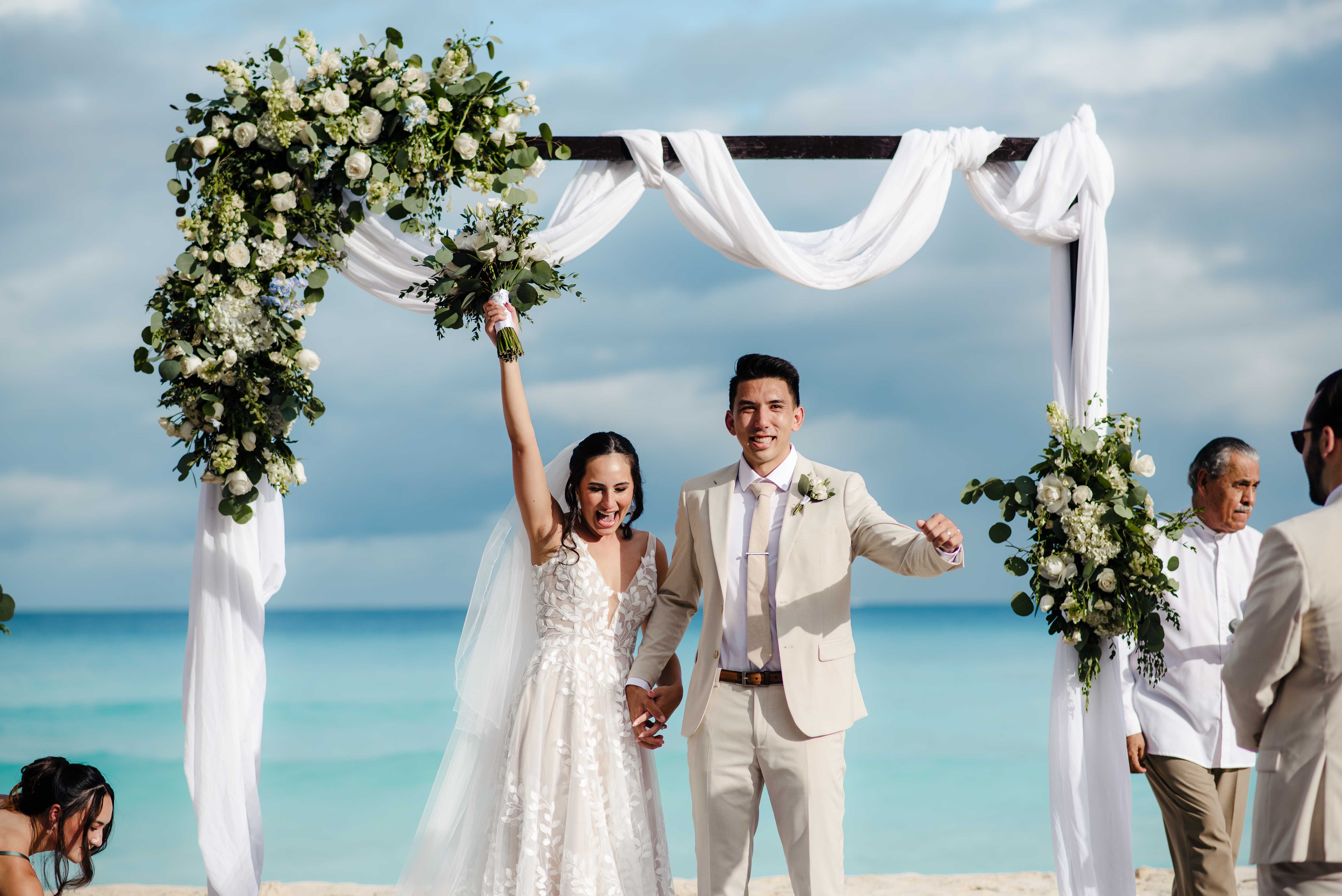 Joyful ceremony exit moment with couple celebrating under floral arch