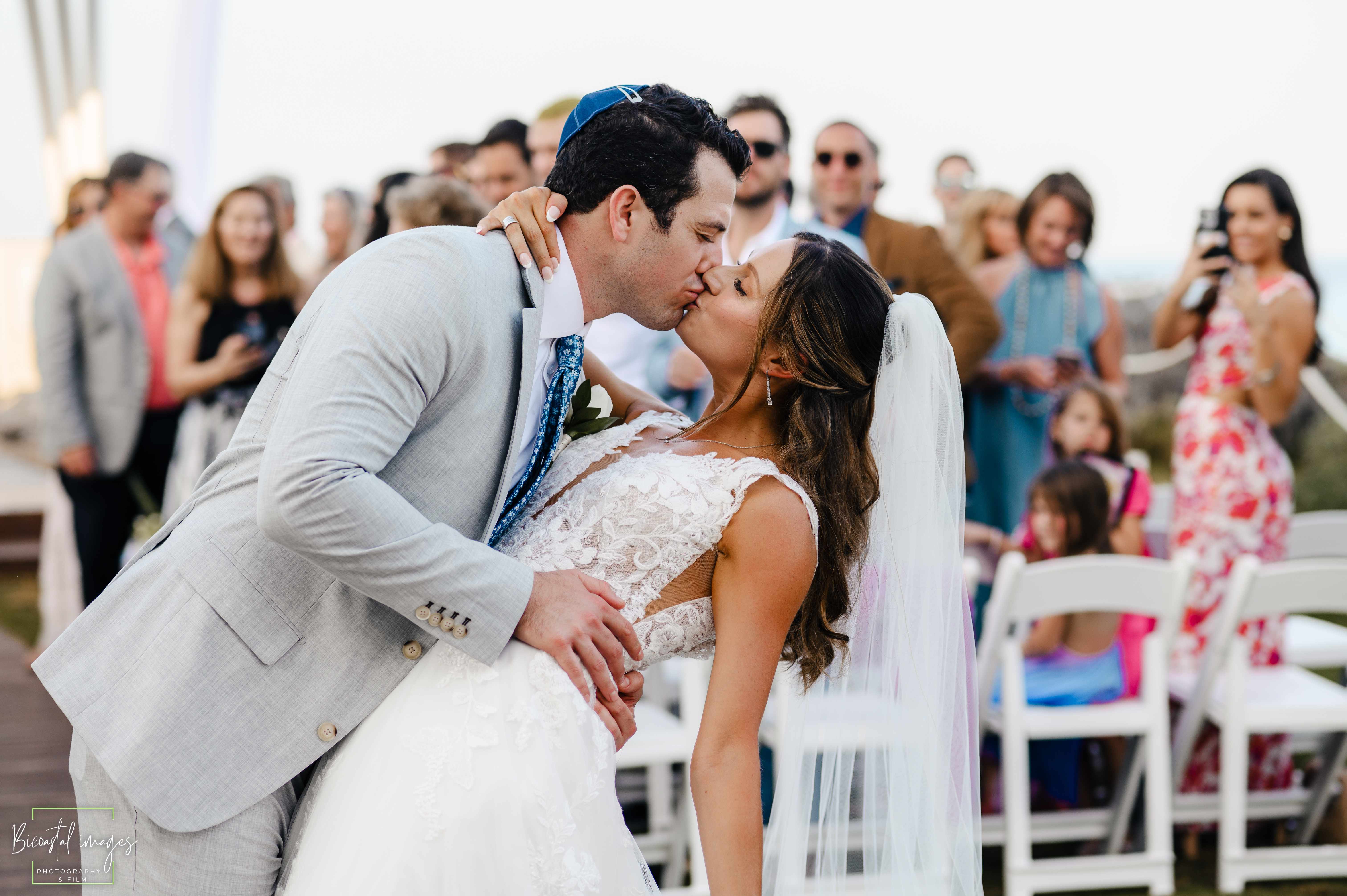 Ceremony kiss moment with wedding party and guests in background