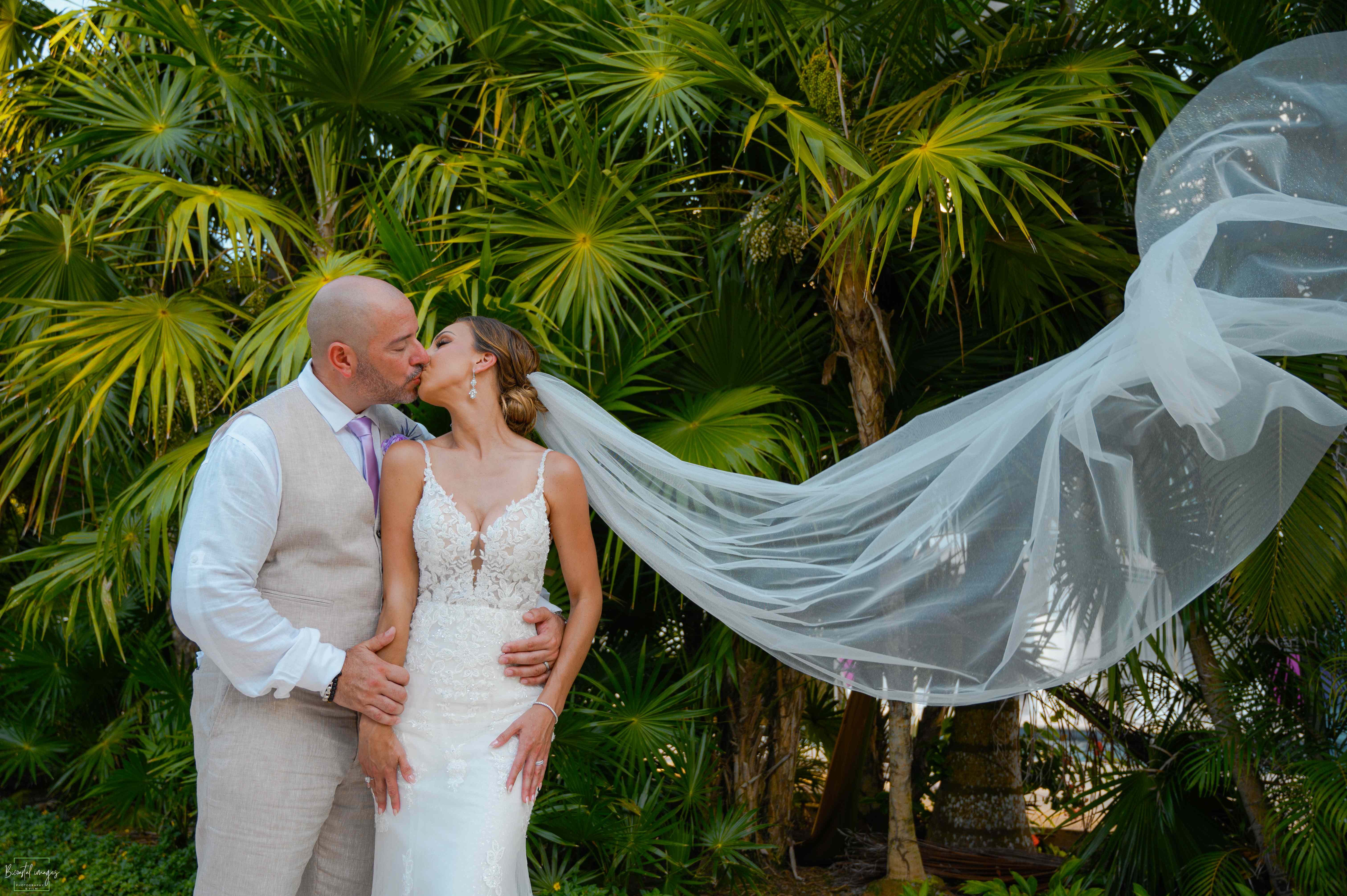 Intimate couple portrait with dramatic flowing veil against tropical palms