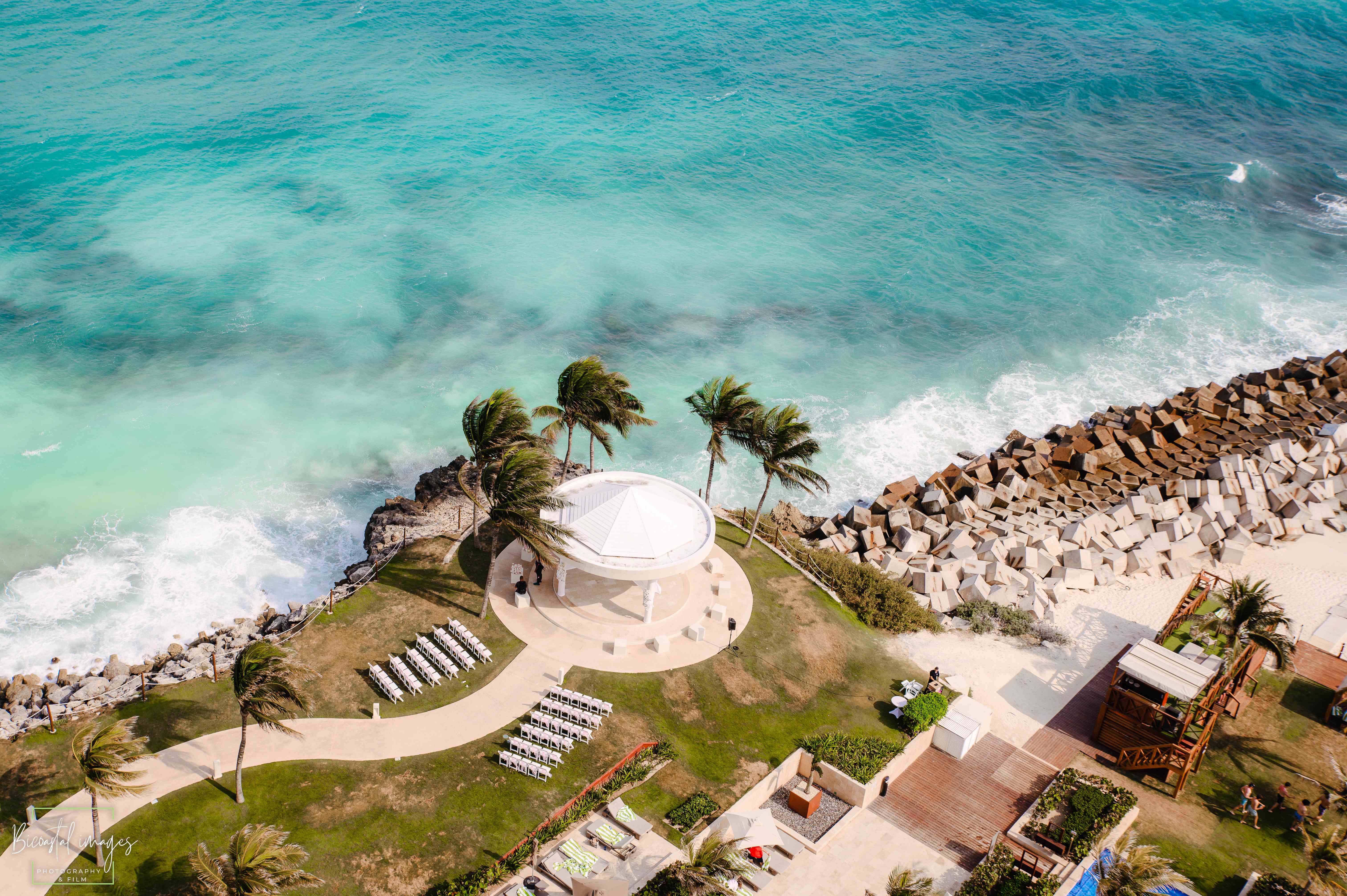 Aerial view of the white domed oceanfront wedding gazebo and ceremony setup on the private peninsula surrounded by turquoise Caribbean water at Hyatt Ziva Cancun photographed by Bicoastal Images