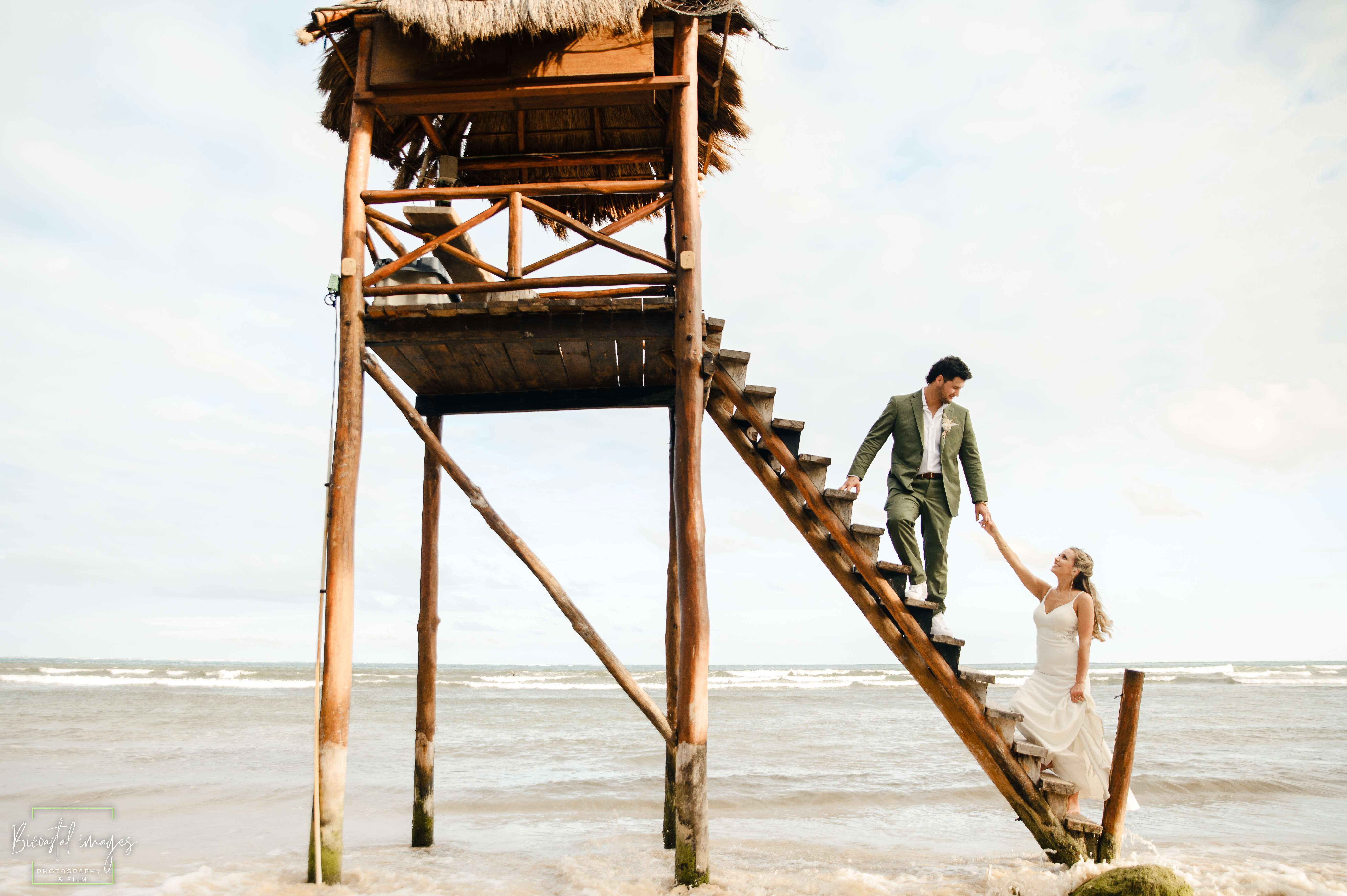 Dramatic couple portrait on wooden lifeguard tower stairs with beach backdrop